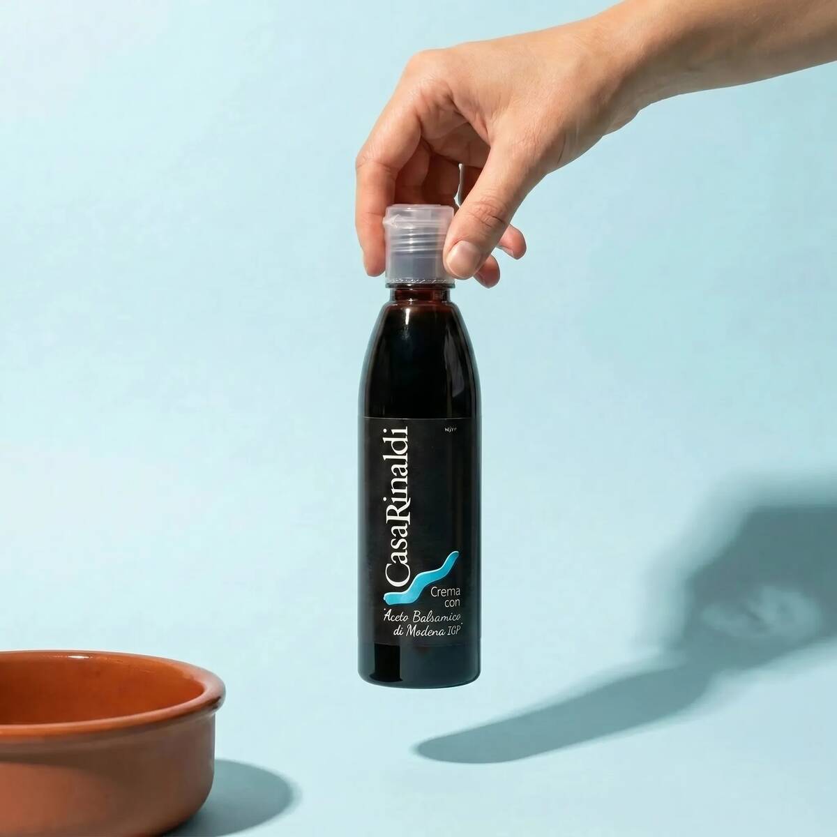 Hand holding a bottle of Casa Rinaldi Balsamic Glaze of Modena PGI 250ml against a light blue background
