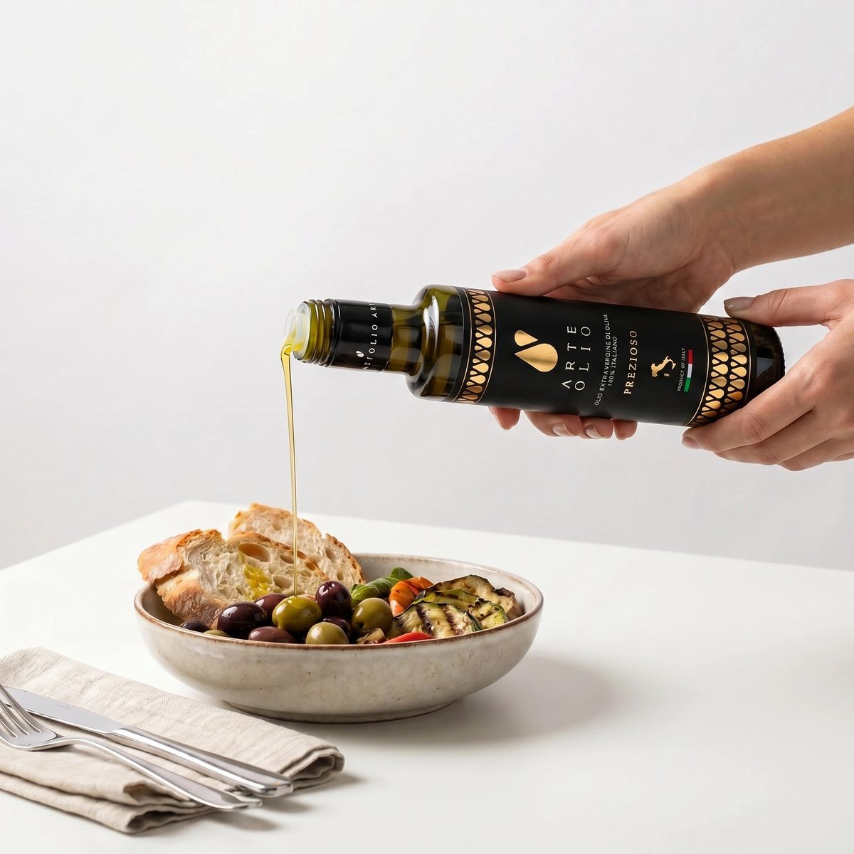 ArteOlio Prezioso extra virgin olive oil being poured over Italian bread and olives in a ceramic bowl